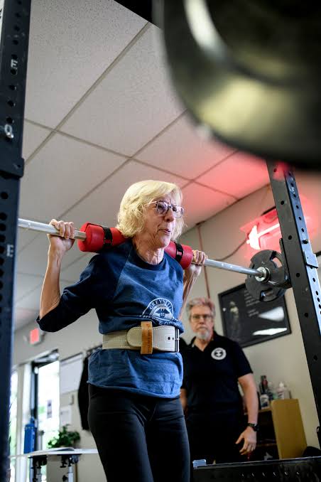 Woman setting up under a barbell for a squat with her coach watching