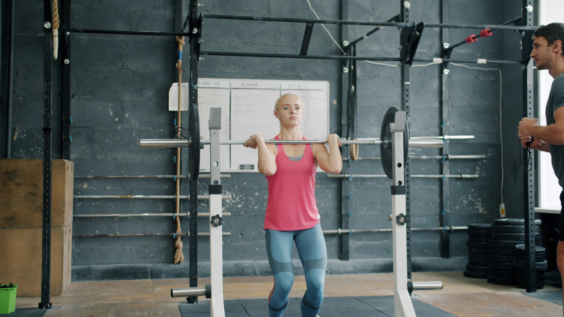 Coach guiding a woman through a barbell lift